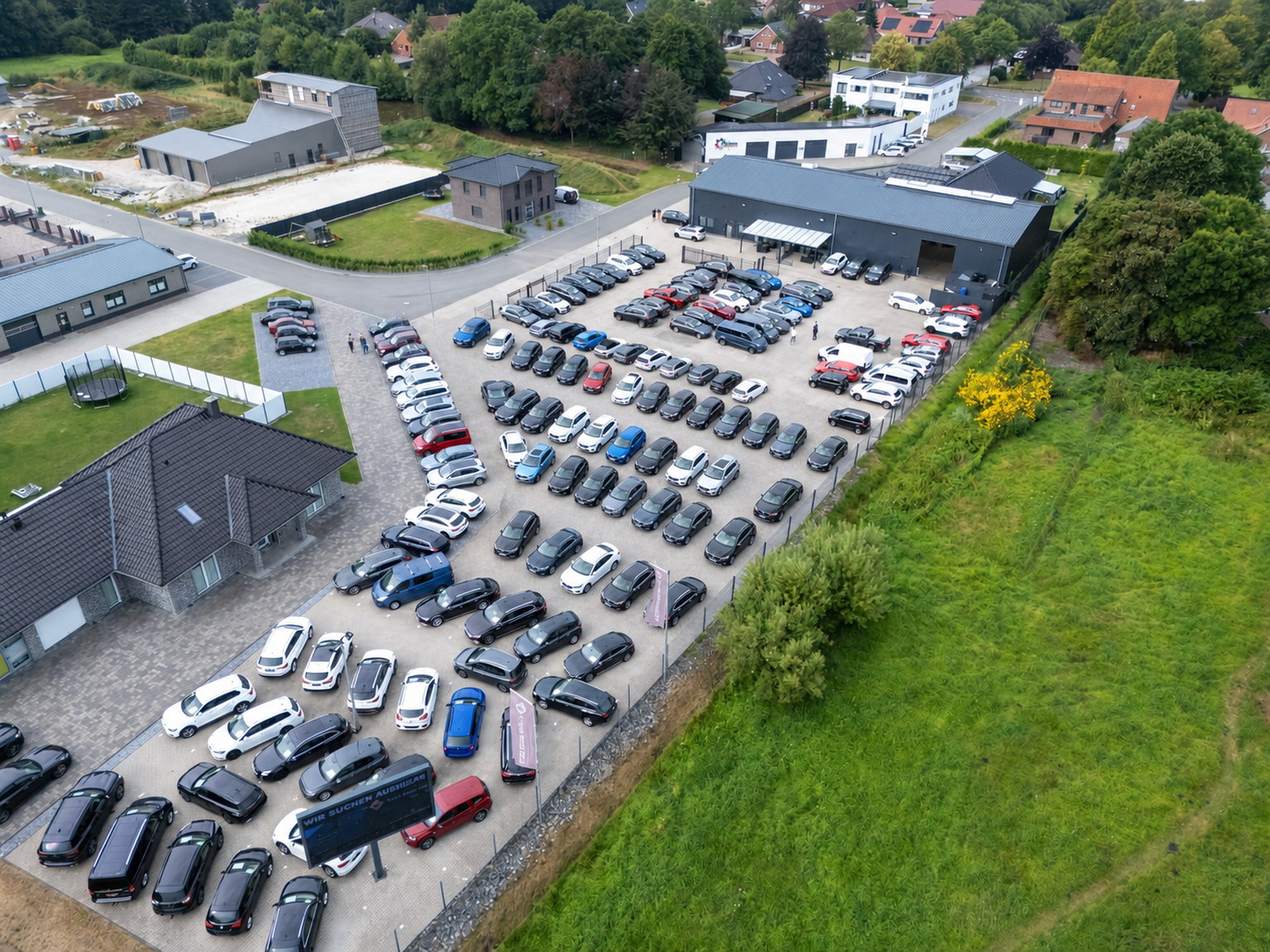 Luftaufnahme des Autohauses Your Next Car mit durchgehender gepflasterter Fahrzeugfläche in Ostrhauderfehn